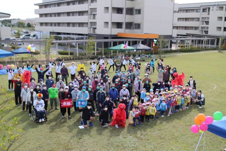 走らないミニ運動会に参加する多くの子どもと大人が芝生の上に集まった記念撮影を上空から写した写真