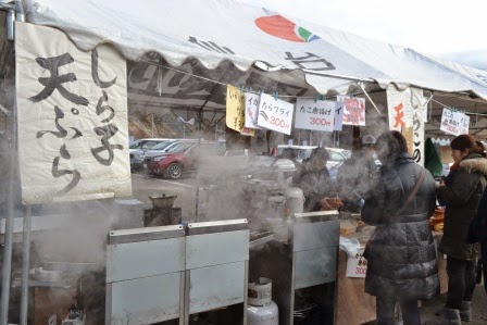 しら子天ぷらやタラフライなどの手書きのポップが貼られた湯気が立ちこめる屋台で、来場者が食べ物を購入している写真