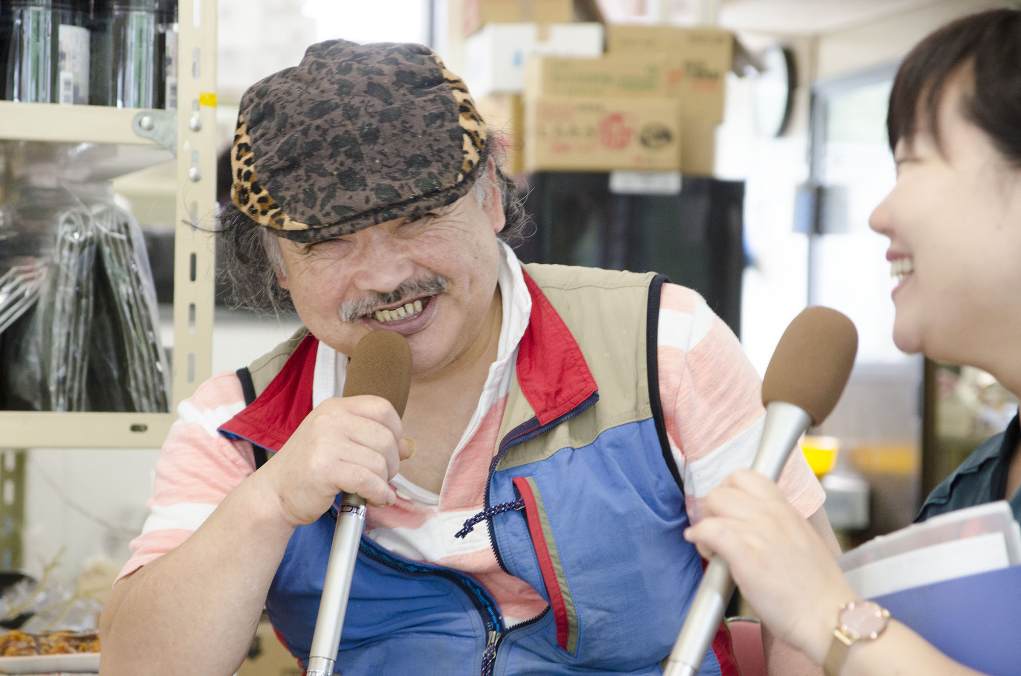 ヒョウ柄の帽子をかぶったベスト姿の三浦保志社長がマイクを持って笑いながら話し、隣でリポーターの女性がもう一本のマイクを持って笑顔で会話をしている写真