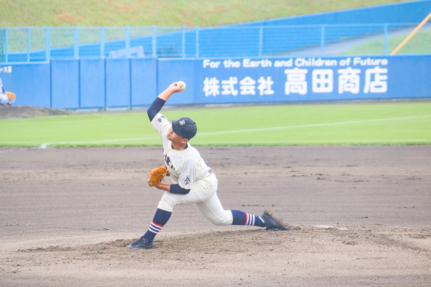 マウンドから投球する白いユニフォームの投手が、腕をぐっと振り上げて力強くボールを投げている瞬間の写真