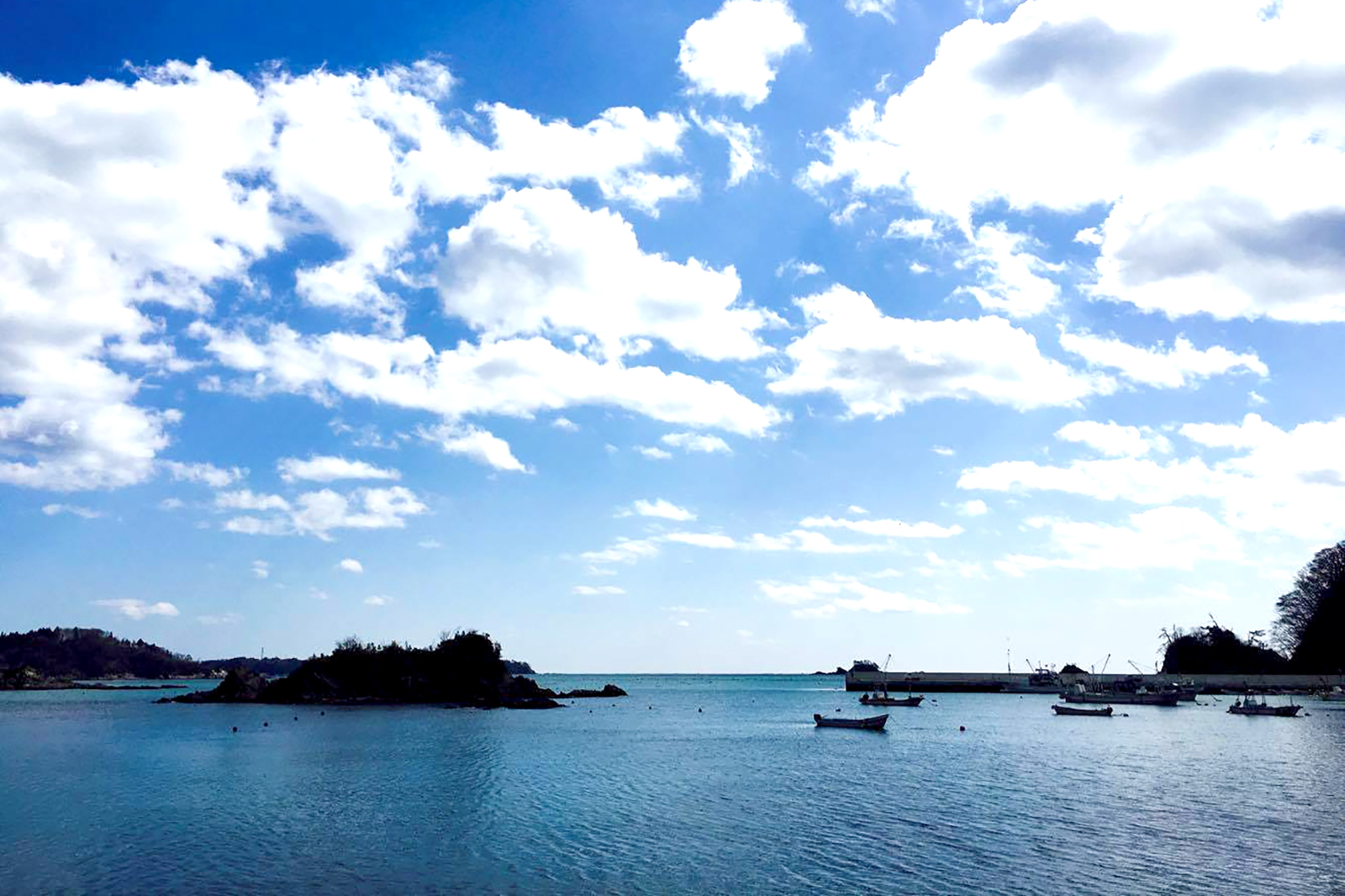 白い雲が浮かぶ青空の下、穏やかな海面に小舟が浮かぶ様子を写した写真