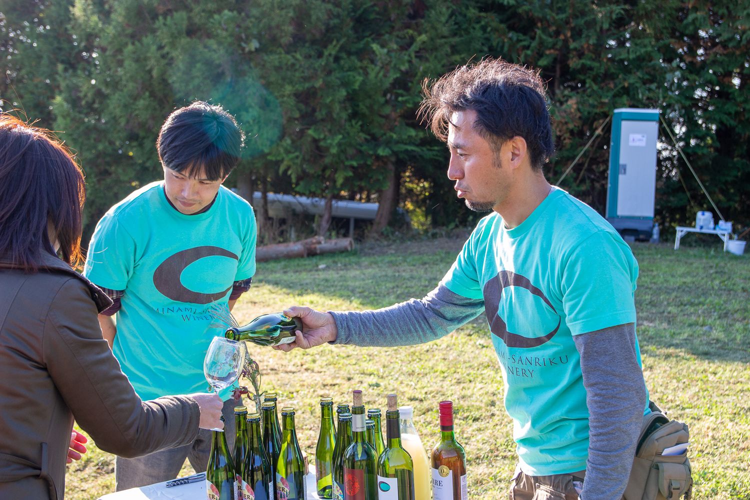 佐々木道彦さんがワインボトルから参加者が持っているグラスにワインを注いでいる様子の写真