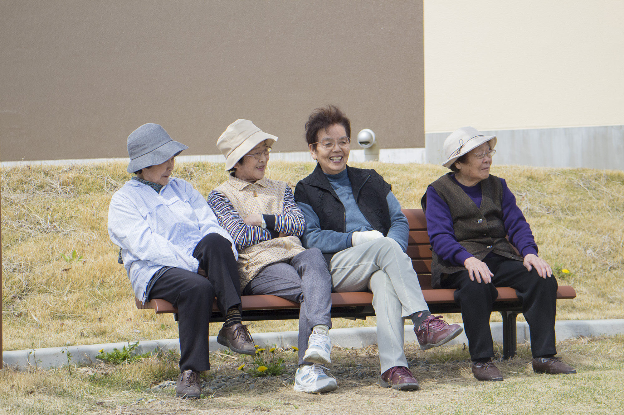 4人の年配の女性たちがベンチに座り笑顔を見せながら談笑している様子の写真