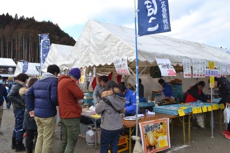 防寒着を着た来場者たちがテントの下の魚介類販売ブースで商品を見たり購入したりしている写真