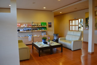 テーブルとソファが置かれたくつろぎスペースに、地域の特産品などが並ぶ棚が見えるロビーの写真