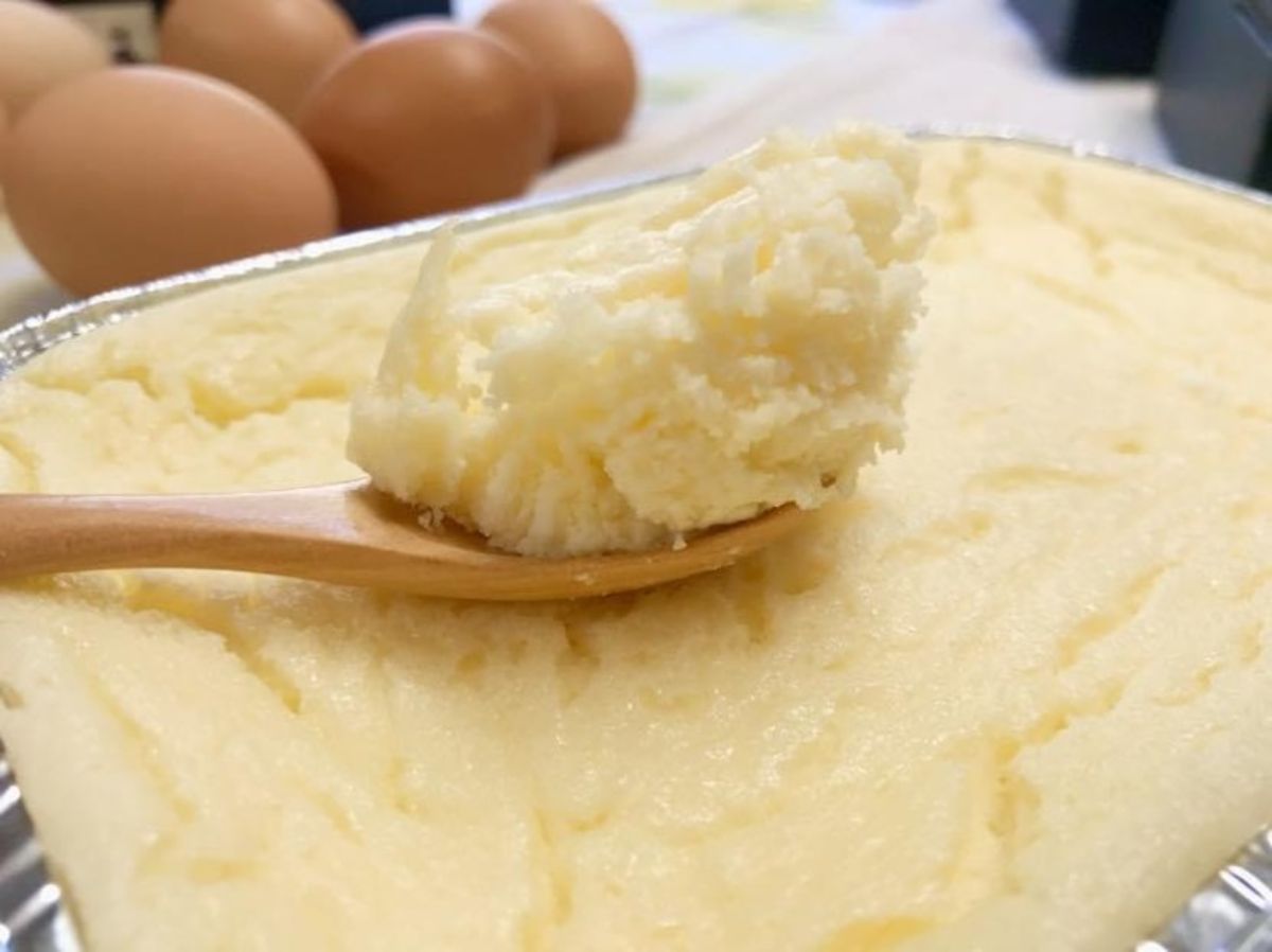 銀色のトレイに入ったふわふわとしたカスタードチーズケーキから木のスプーンですくい取った様子がアップで写されている写真