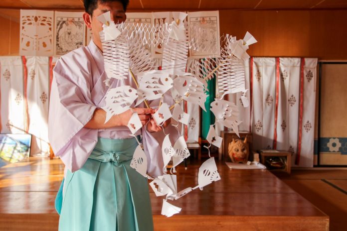 白衣と袴を着た工藤庄悦さんが竹の棒に刺さった「きりこ」を持っている写真