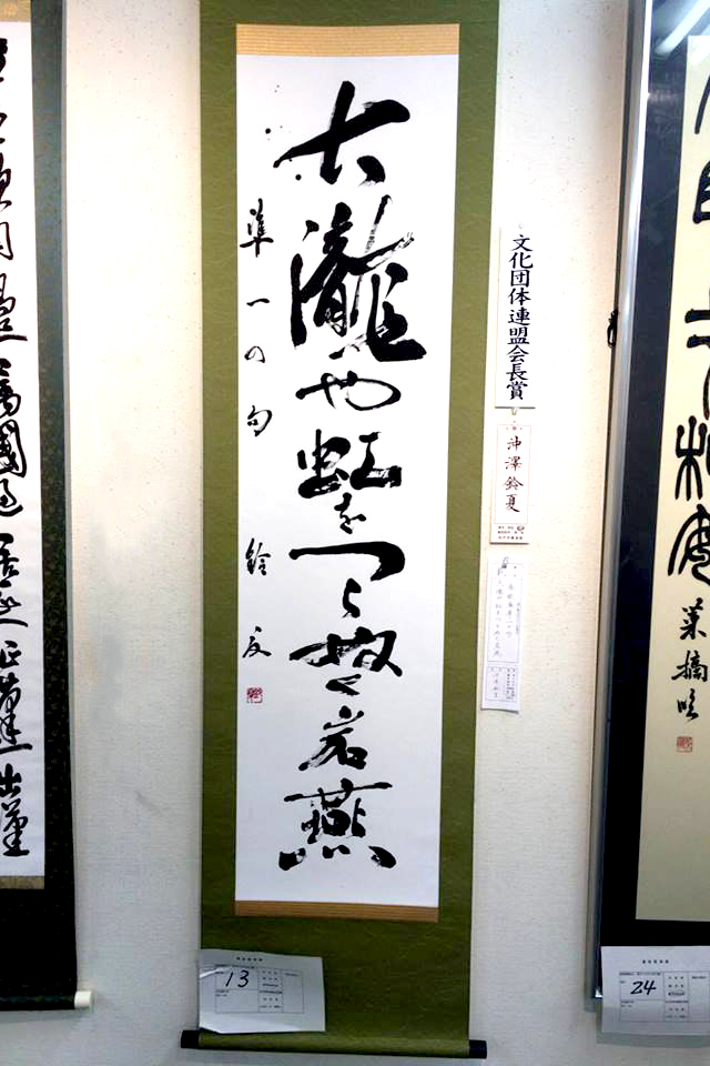 掛け軸に力強い筆致で書かれた書道作品を展示している写真