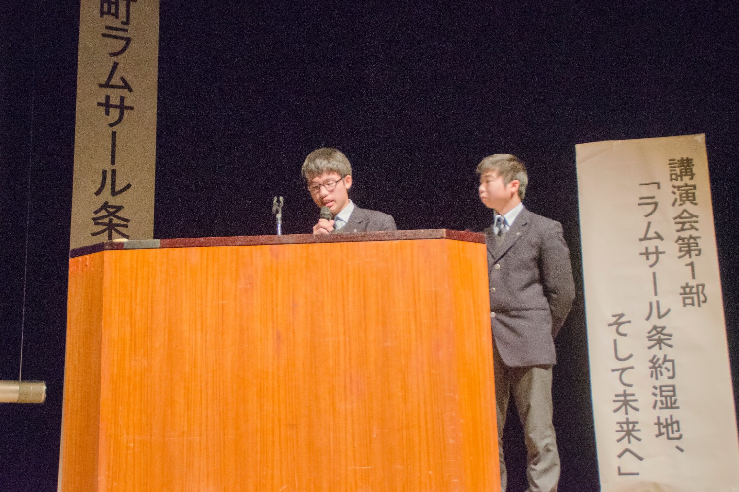 シンポジウムで壇上で、志津川高校自然科学部の二人の学生が発表をしている様子の写真