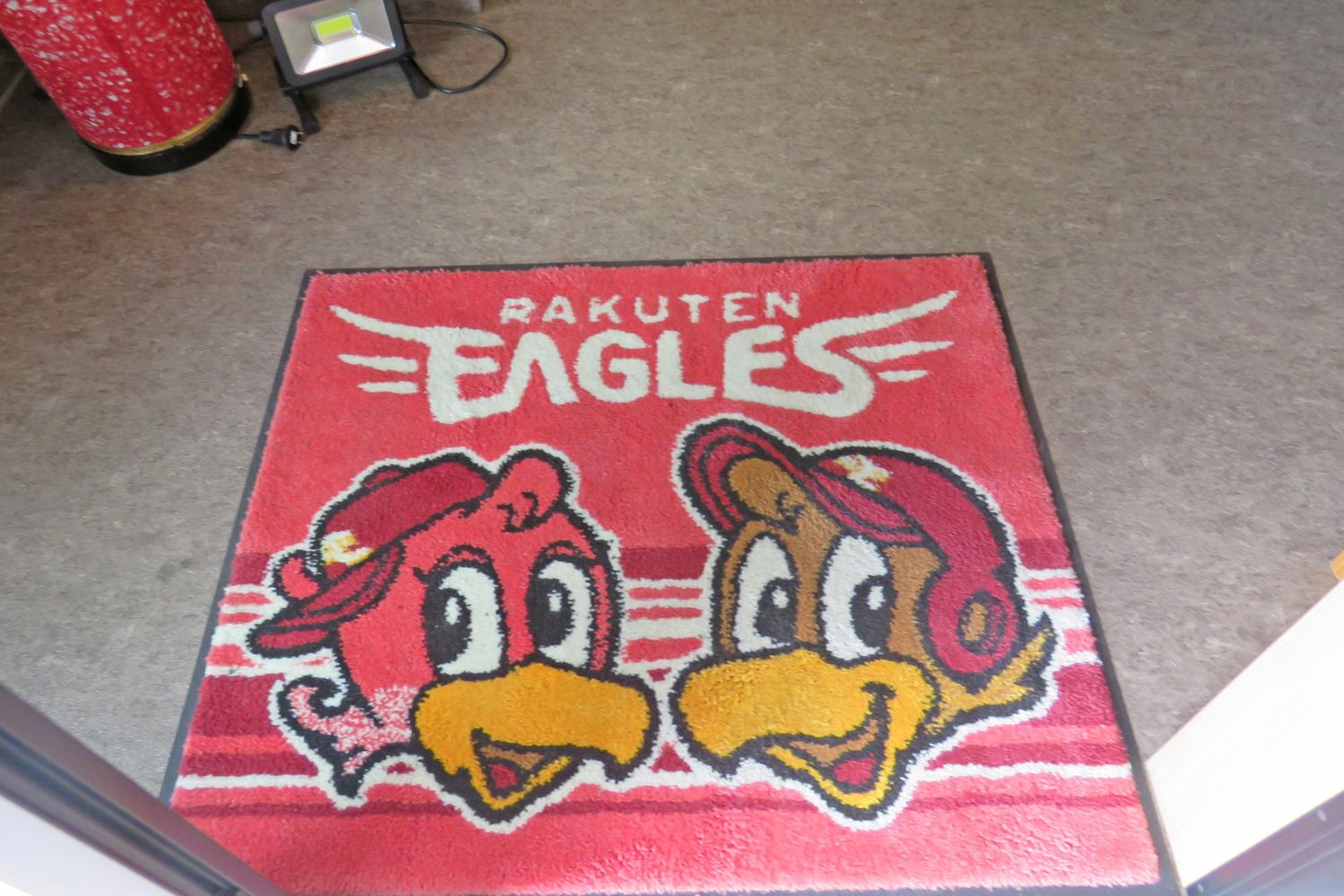 白い文字で「RAKUTEN EAGLES」と書かれ、楽天イーグルスの2羽の鳥のキャラクターが描かれている赤い床マットの写真