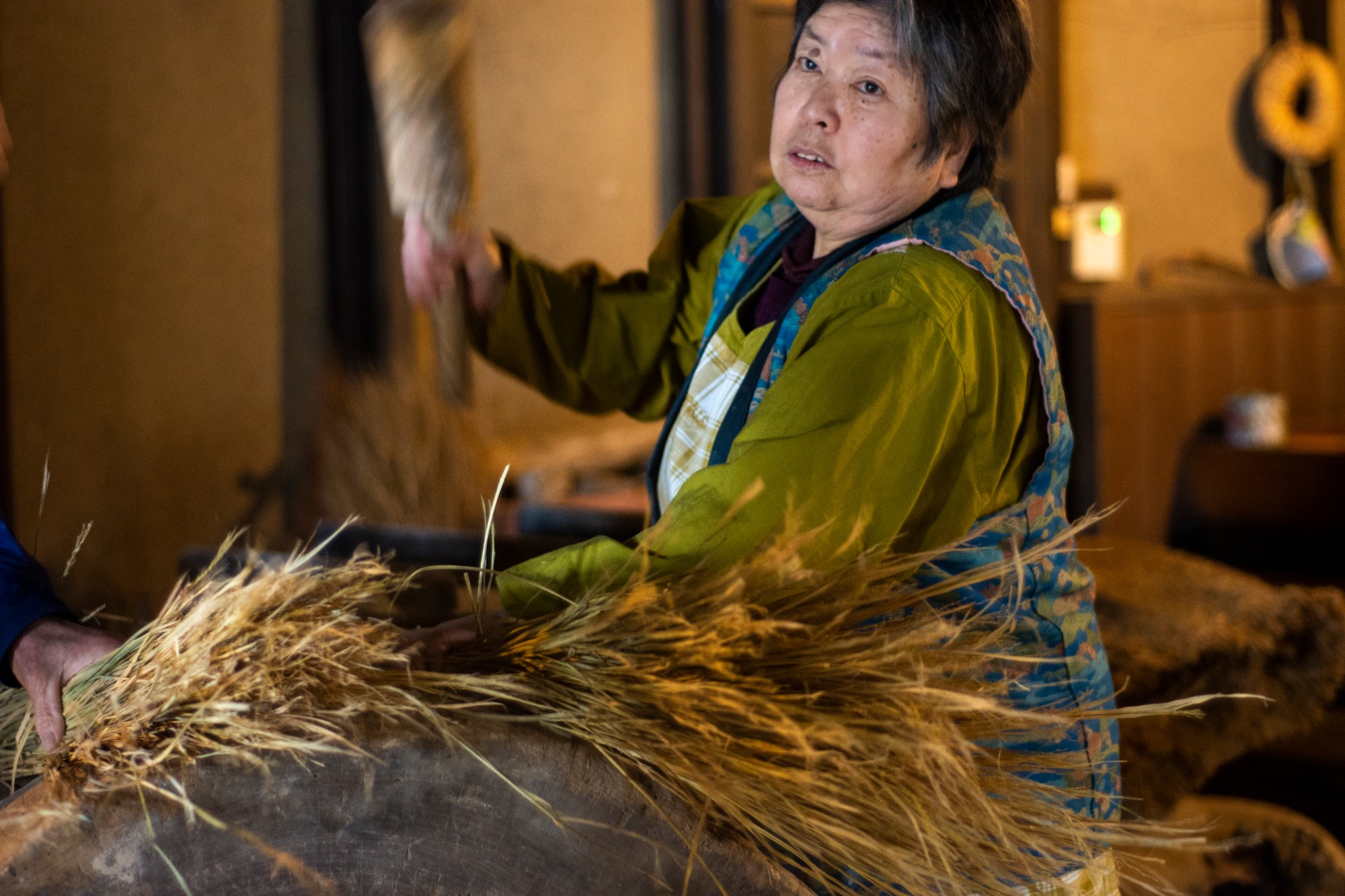 女性が木槌を振り上げ藁を叩いている作業の様子を写した写真