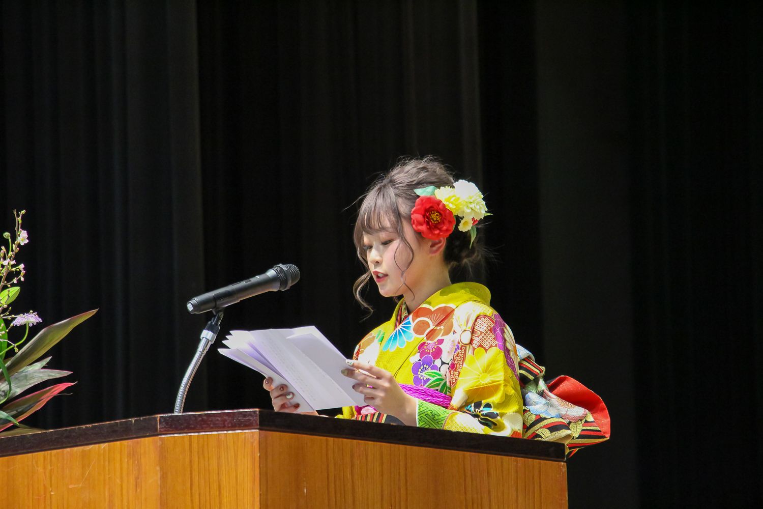 黄色の華やかな着物を着た畠山史花さんがマイクの前に立ち、抱負を読み上げている写真
