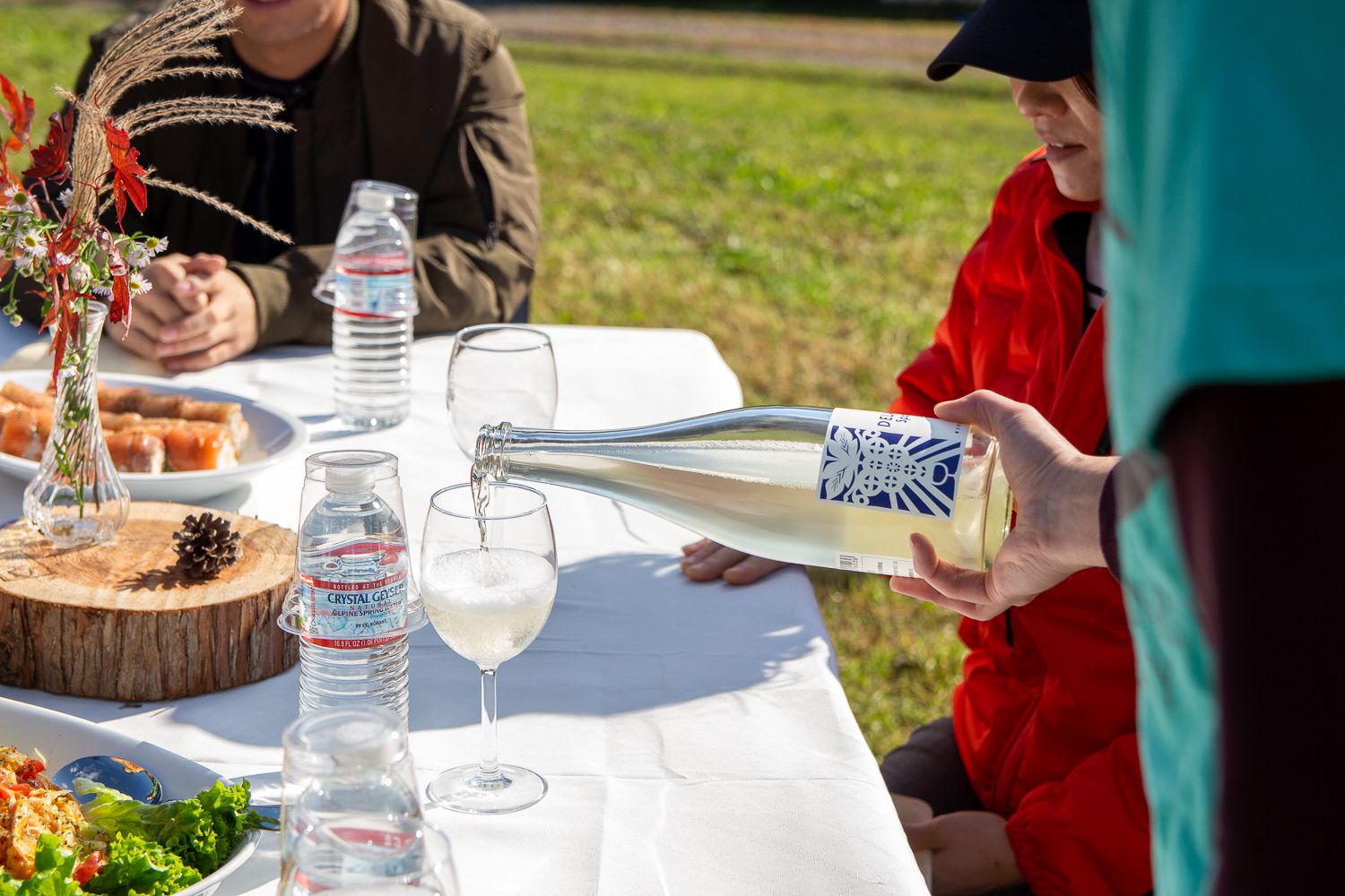 白いテーブルの上に置かれたグラスにスパークリングワイン注いでいる手元の写真