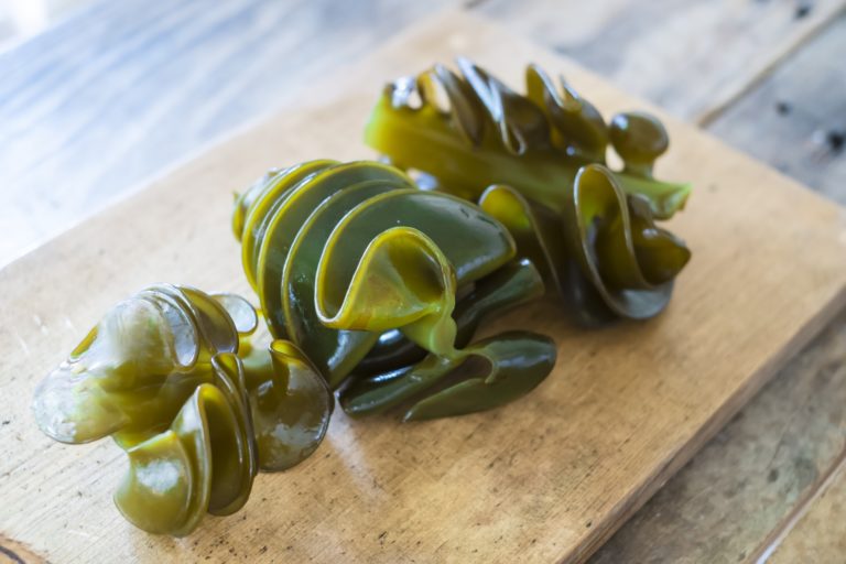 木製のまな板の上に、緑色で光沢のあるメカブが三つ並んでいる写真