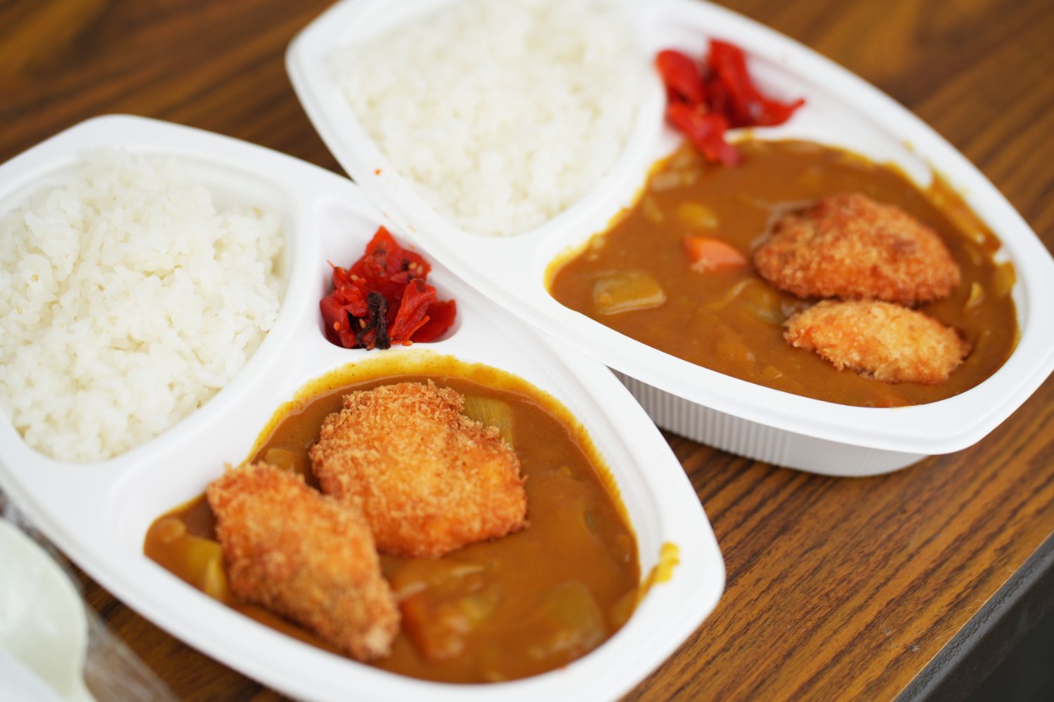 白い仕切り付き容器に盛られた揚げ物がのった具だくさんのカレーライスと福神漬けが並び、ツール・ド・東北の参加者に提供された温かい昼食の一例を示す写真