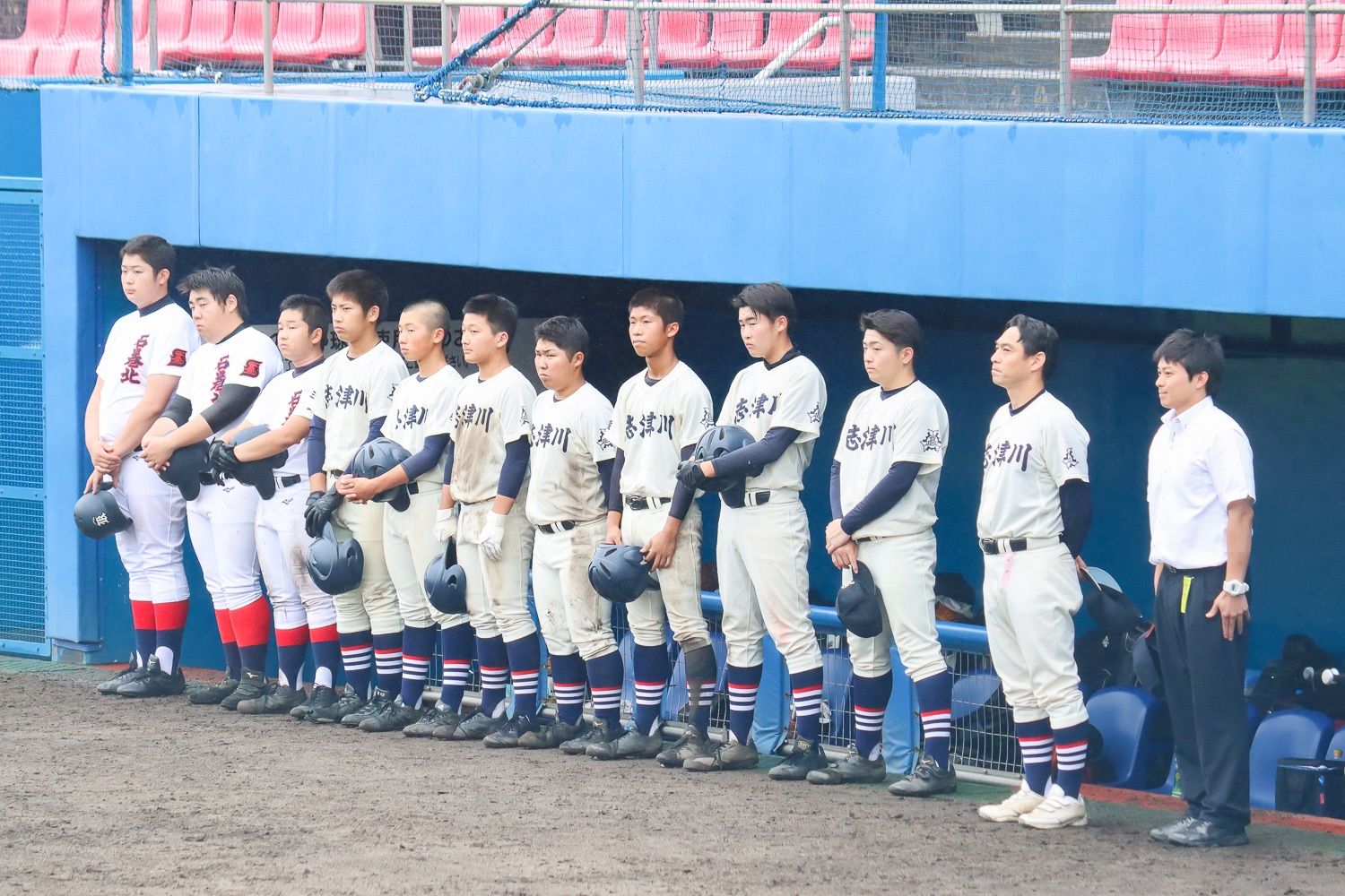 「志津川」と書かれた白いユニフォーム姿の野球チーム員が帽子を手に持ち並んでいる写真