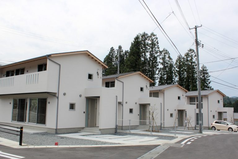 緩い傾斜のある坂道沿いに、駐車場が完備された白壁の2階建ての住宅が4棟建っている写真