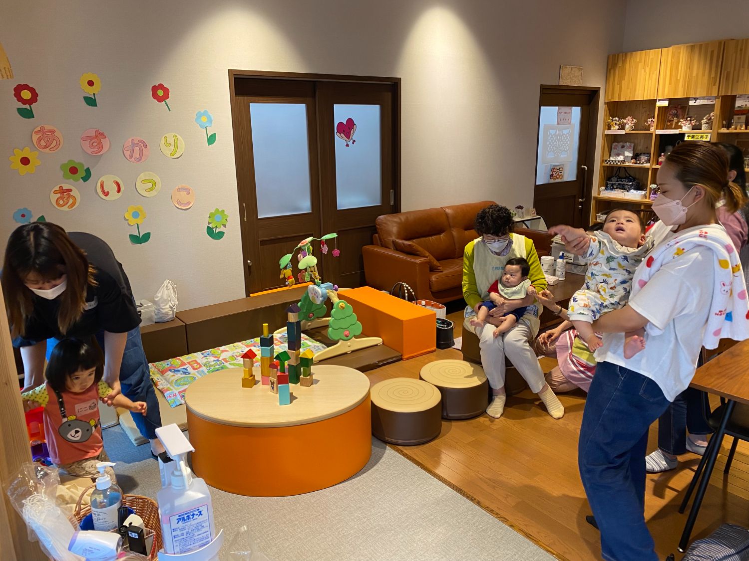 赤ちゃんを抱いた母親と小さな子どもたちが遊具のあるスペースで過ごしながら交流している写真