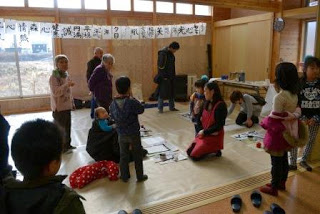 子どもたちと地域の大人たちが室内に集まり、正月の習字体験を通して交流を楽しんでいる様子を写した写真