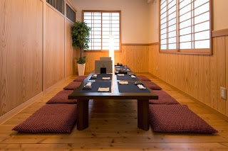 木の壁と障子に囲まれた和室に赤い座布団が並べられ、中央に長いテーブルと箸や器が整然と並ぶ個室の写真