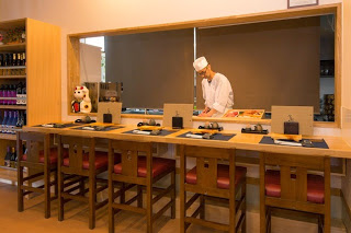 カウンター席の向こうで寿司職人が握っている様子が見え、椅子が5脚並ぶ清潔感のあるカウンターの写真