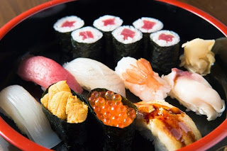 赤い縁の丸い器に鉄火巻きやウニ、イクラ、エビなど様々な寿司が美しく盛られた握り寿司の写真