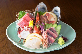 緑の皿にマグロ、カツオ、ホタテ、エビなどの刺身が大葉などと共に彩りよく盛られた刺身盛り合わせの写真