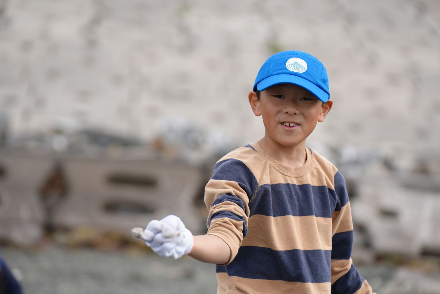 縞模様の長袖シャツを着た少年が白い手袋で小さな生き物を持ち上げ、笑顔で見せている様子の写真