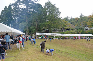 広場の斜面に設置された白いテントの下に多くの人が集まり、屋台やイベントを楽しんでいる様子の写真