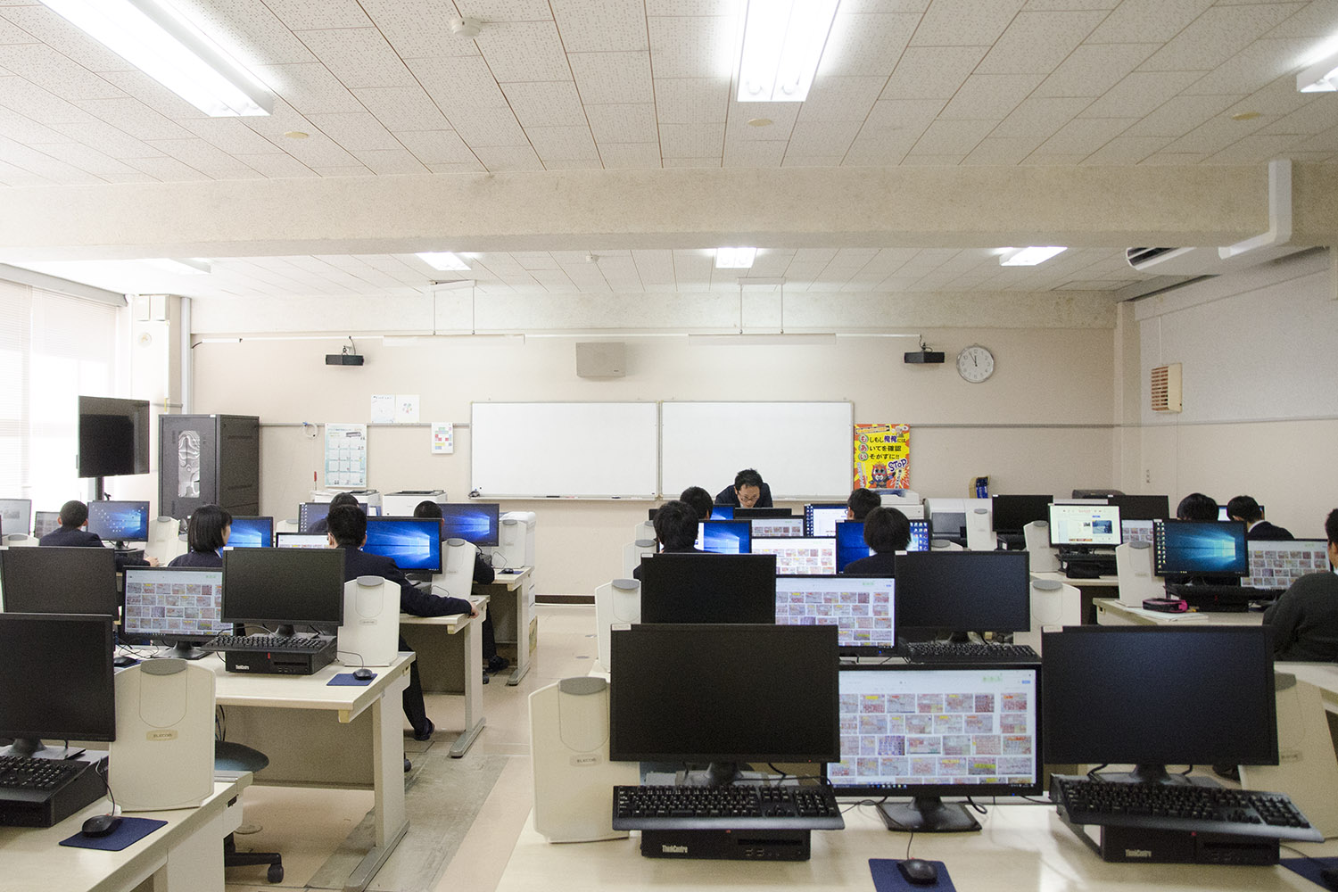 前方にホワイトボードがある教室内にはパソコンが設置された机が複数並び、取引画面が映し出されたモニターを見ながら、多数の生徒がそれぞれのパソコンを使い、教師の指導のもとで授業を受けている様子の写真