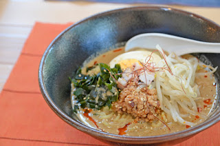 濃いスープにゆで卵、もやし、ひき肉、わかめなどの具材が盛りつけられた担々麺がオレンジのランチョンマットの上に置かれている写真