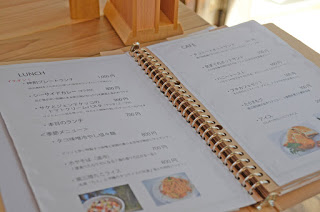 リング式バインダーに綴じられたメニューが開かれており、ランチやカフェの料理名と価格、写真が見える写真