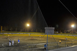 暗闇の中ナイターの光で照らされた球場で野球を楽しんでいる人たちの写真