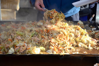 鉄板の上で大量の野菜など炒めている様子が写されており、湯気が立ちのぼる熱々の料理をヘラでかき混ぜている調理中の様子をアップで撮影した写真