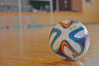 白を基調に青・緑・オレンジの模様が入ったサッカーボールが木製の屋内コートの上に置かれている様子をアップで撮影した写真