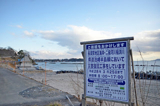 海岸近くの道路に大きな災害復旧工事の案内看板が立っている様子の写真