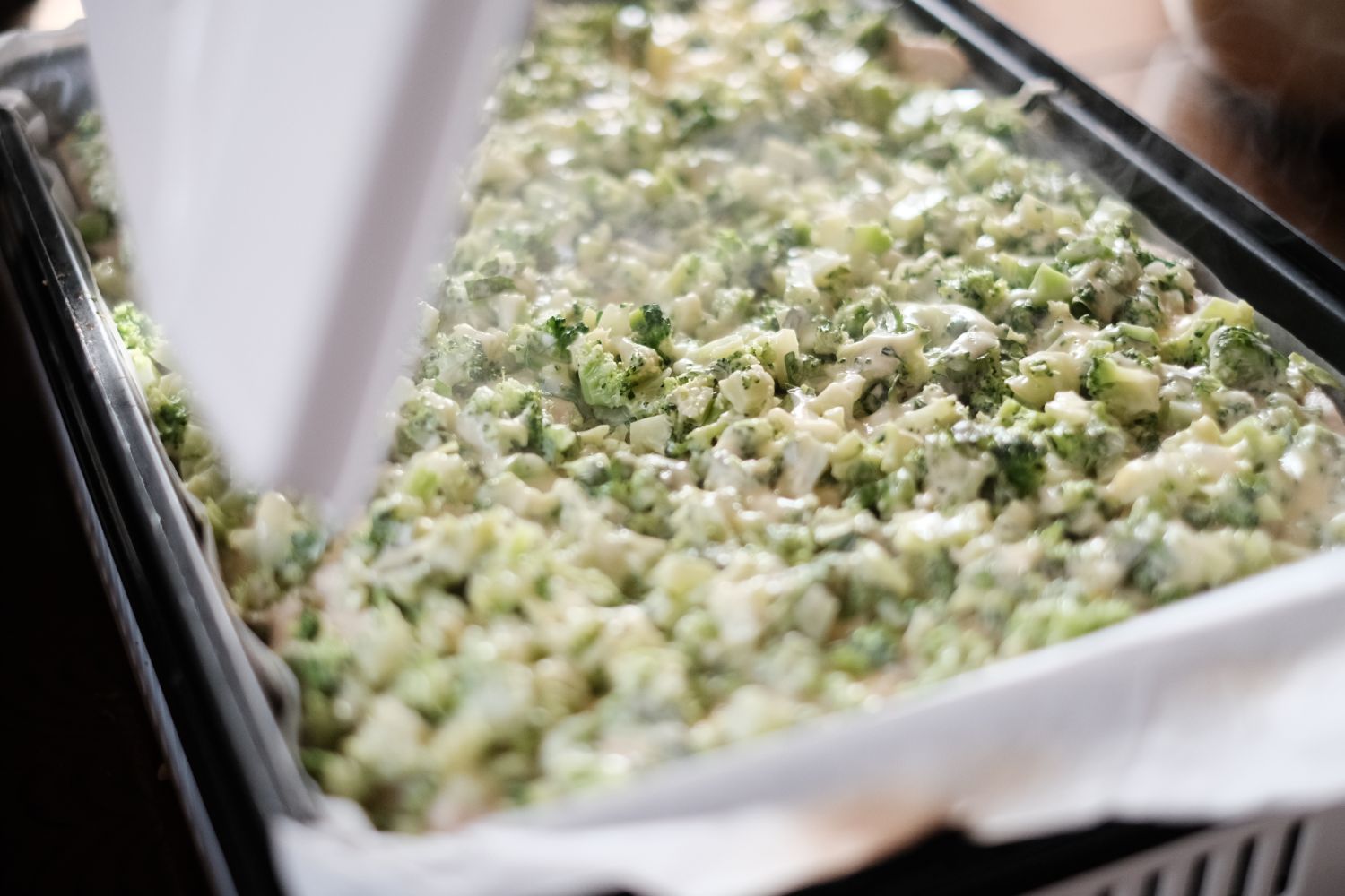 天板の上にクッキングシートを敷き、トウキの葉を細かく刻んで他の具材と混ぜて広げ、オーブンで加熱した直後の湯気が立ち上っている様子を写したトウキ料理の写真