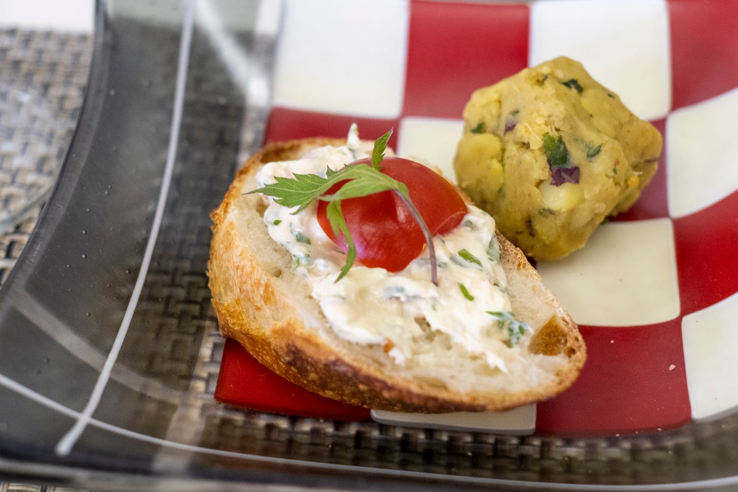 バゲットの上にトウキの葉を混ぜた白いリエットとプチトマトに葉を添えた前菜と、さつまいもとトウキの葉を練りこんだボール状のスパイシーペーストの写真