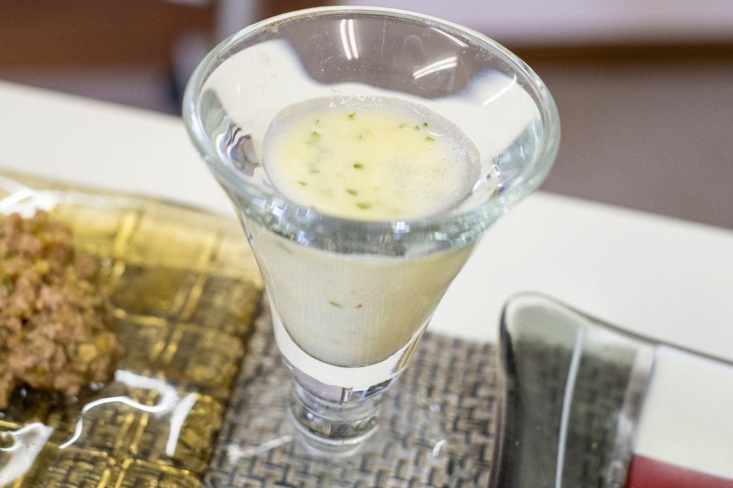 淡い黄色のドリンクに細かく刻まれたトウキの葉が浮かび、ガラスの器に注がれて清涼感を感じさせるトウキ葉のヒーリングドリンクの写真