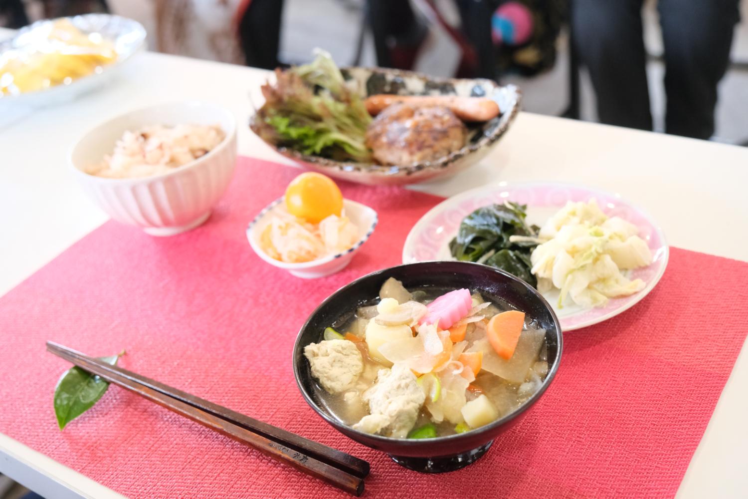 赤いテーブルクロスの上に、並べられた地域の手料理の写真