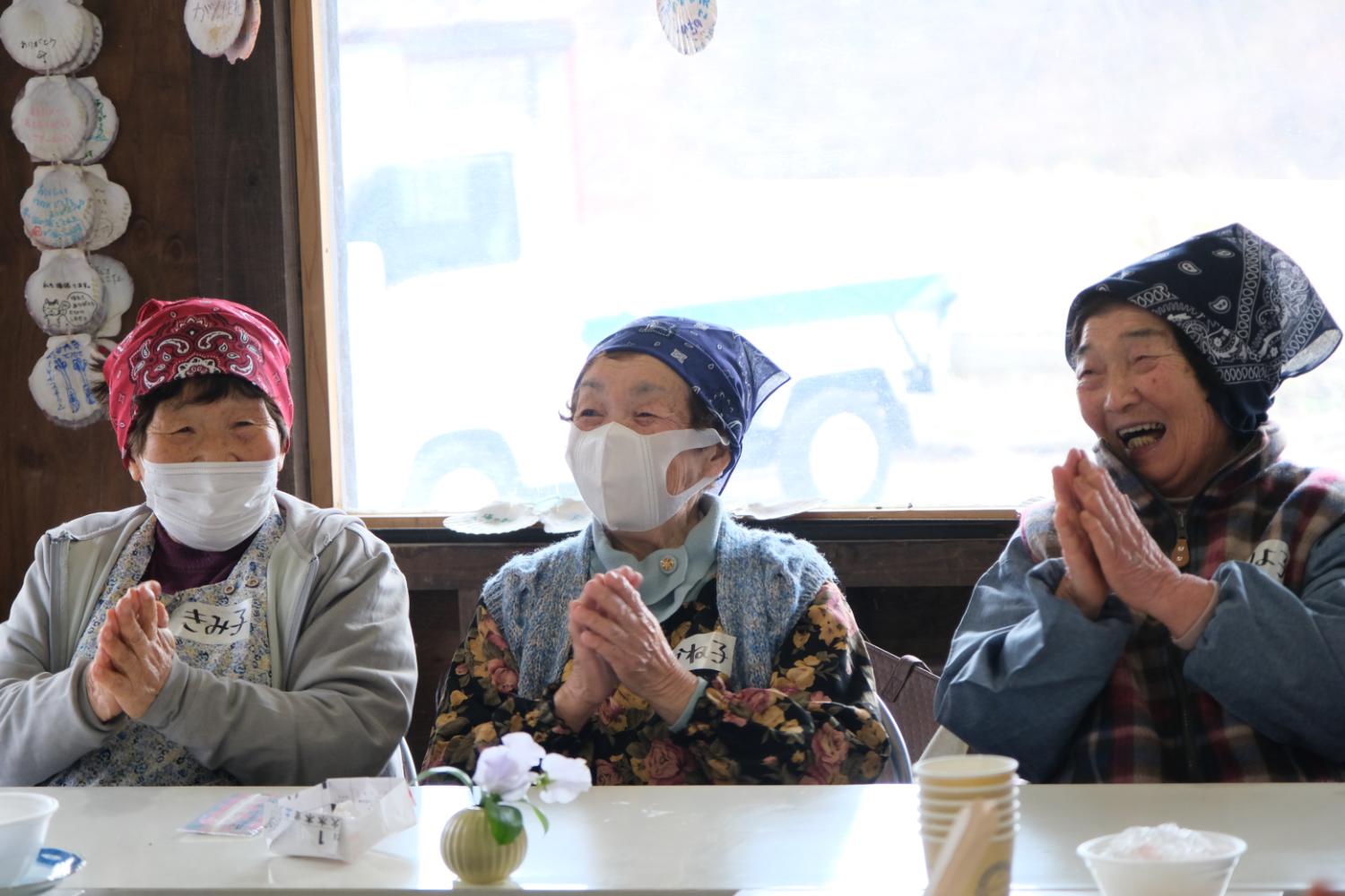 女性3人が頭にバンダナを巻き、楽しそうに笑いながら手を合わせている様子の写真