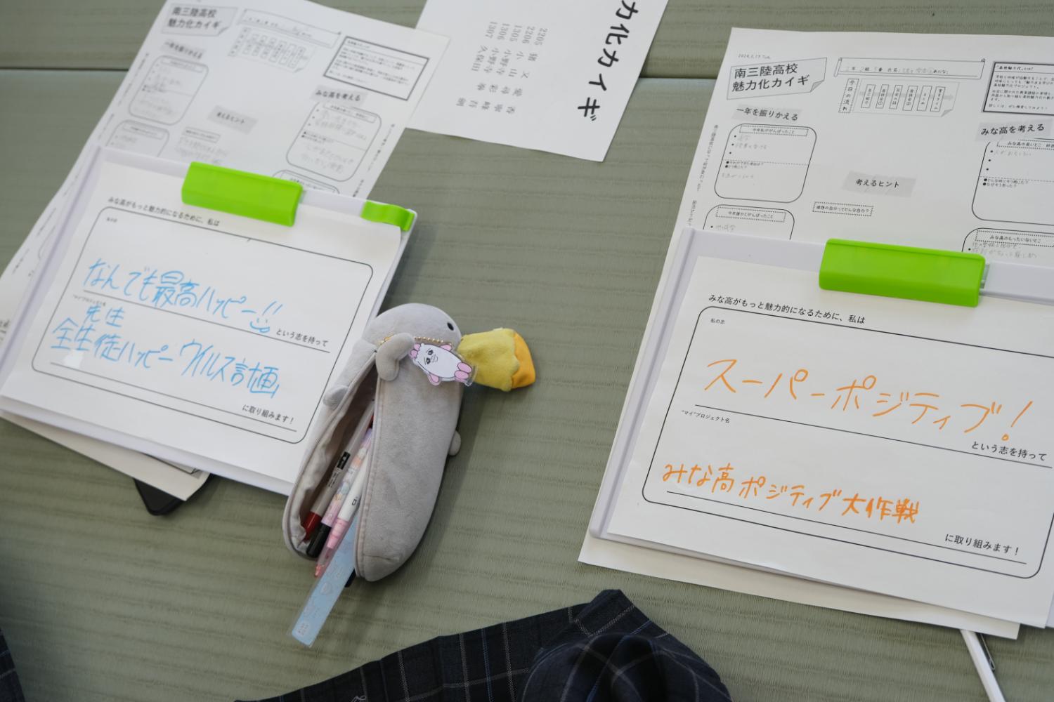 畳の上に広げられた「南三陸高校魅力化カイギ」の用紙に、生徒が色ペンで「なんでも最高ハッピー」「スーパーポジティブ!」などと記入し、ペンケースや文房具がそばに置かれている様子が写っている写真