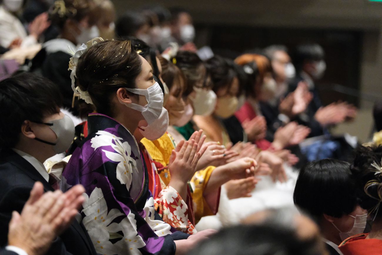 式典中、振り袖姿の成人者たちがマスクを着用しながら拍手を送っている様子を横から撮影した写真