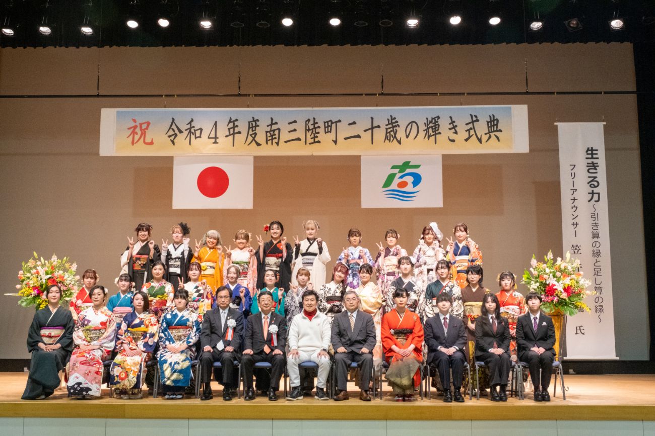 「令和4年度南三陸町二十歳の輝き式典」と書かれた横断幕が掲げられ、振袖姿の女性が多く写っている成人式の集合写真