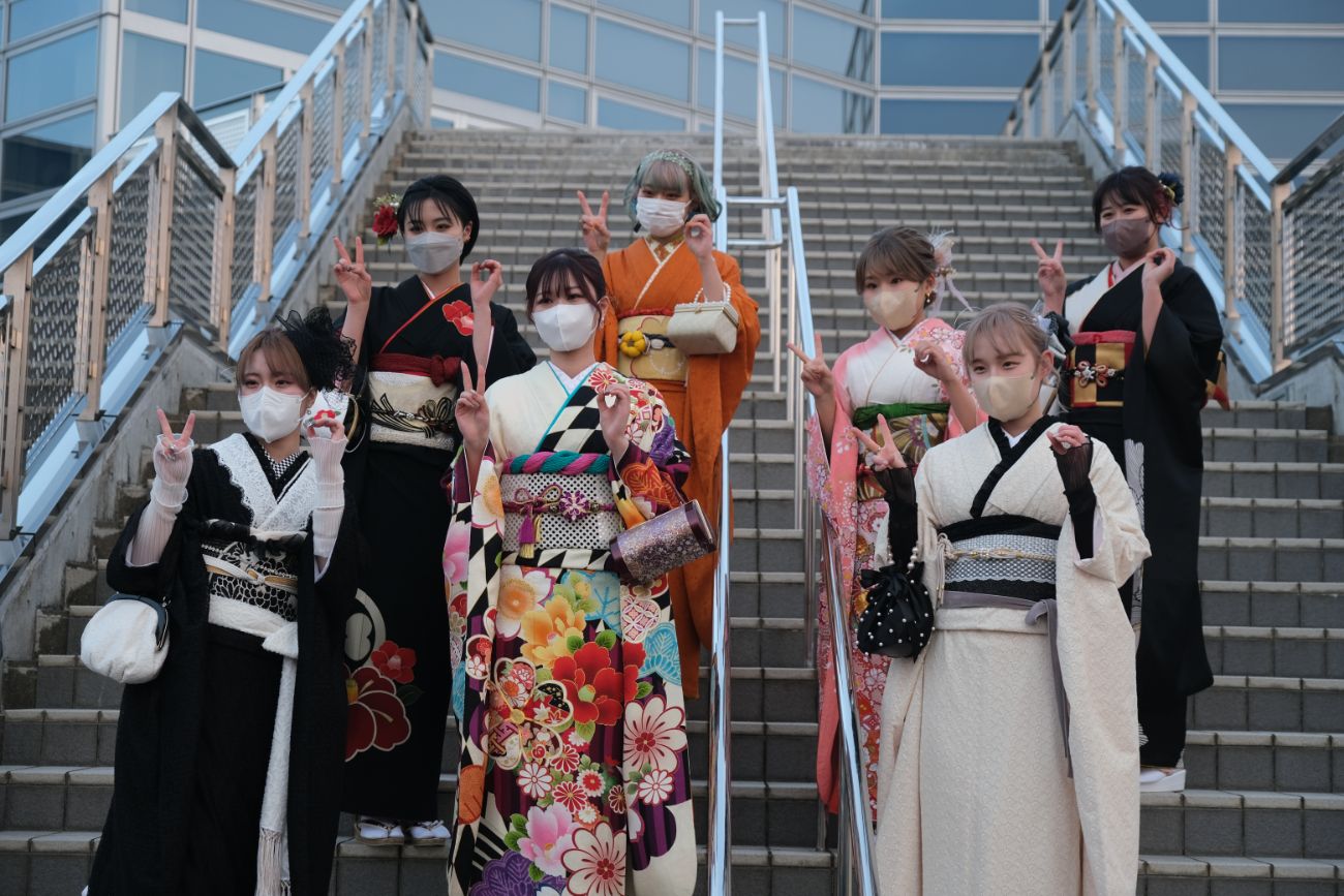 色とりどりの振袖を着た女性たちが階段に並び、笑顔でピースサインをしている様子の写真