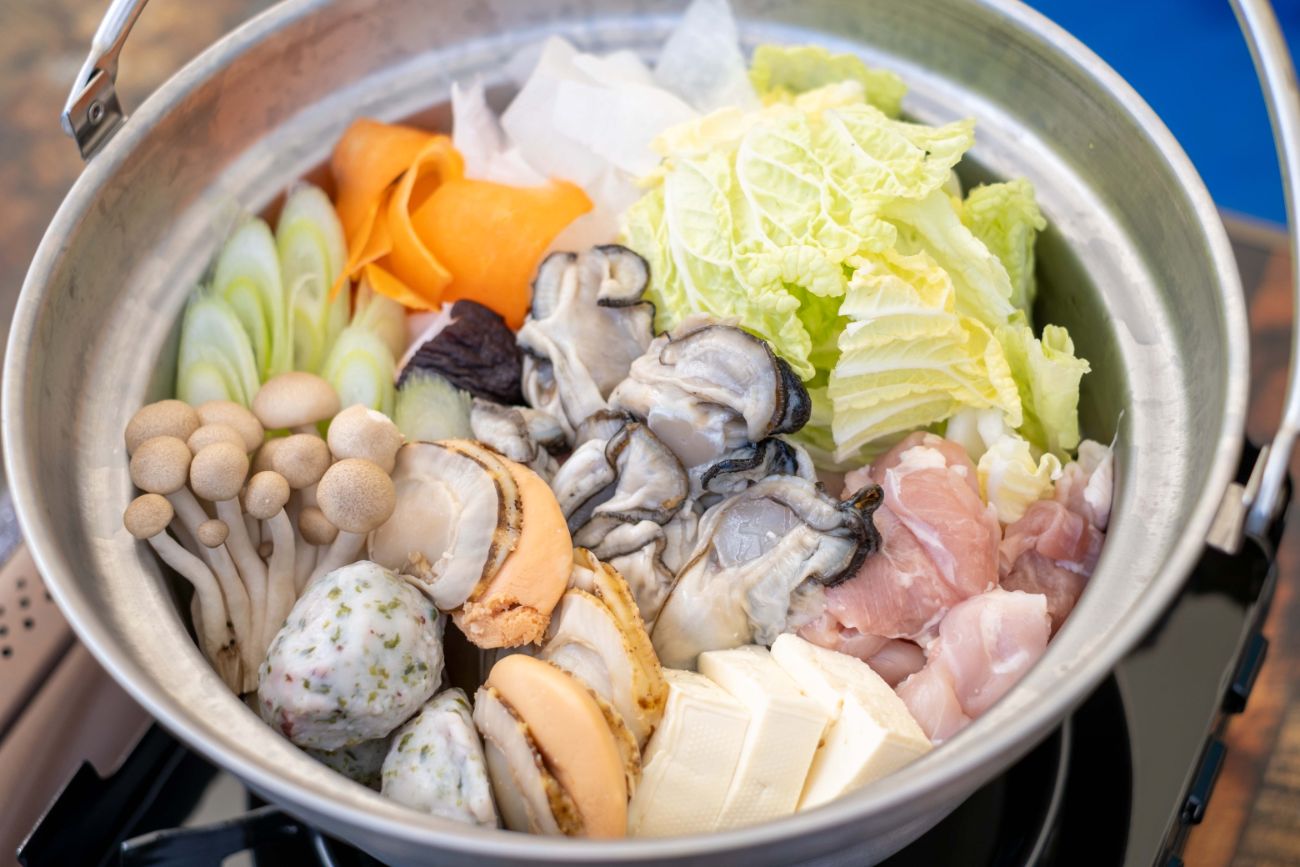鍋の中に白菜、にんじん、ねぎ、シメジ、ホタテ、カキ、鶏肉、豆腐、つみれがきれいに並べられている鍋の写真