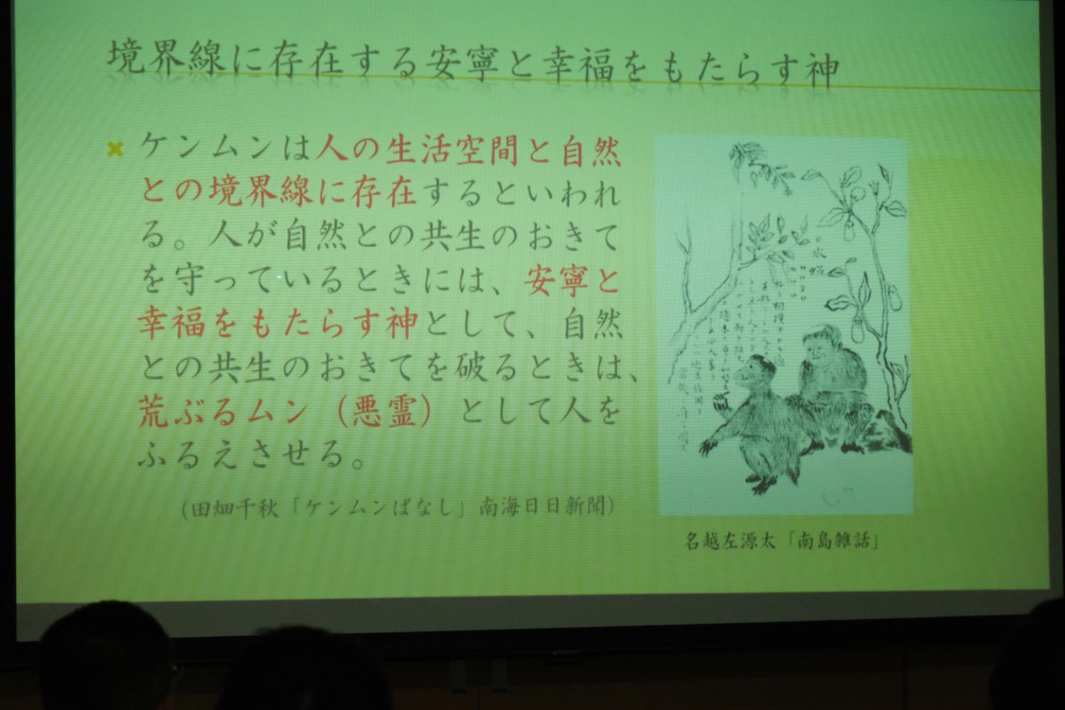 スクリーンに「境界線に存在する安寧と幸福をもたらす神」と題された文章とケンムンのイラストが映し出され、ケンムンについて説明する写真