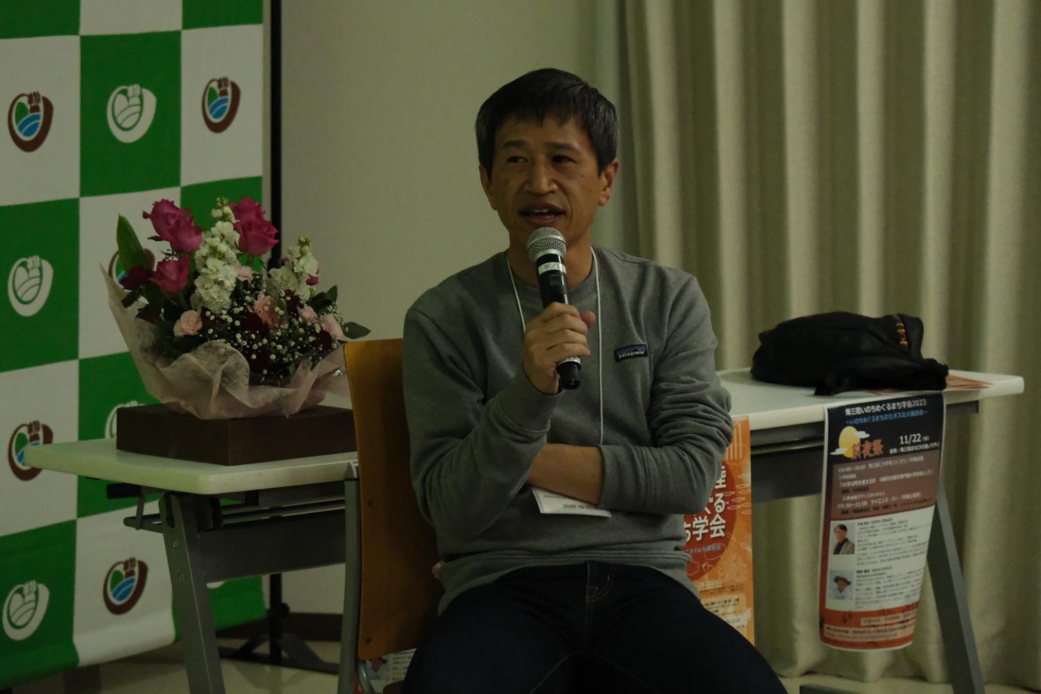 椅子に座ってマイクを持つ岡野さんが話している講演会の写真