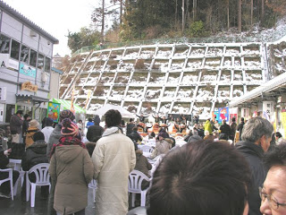 屋外に設置された飲食ブースに設置された椅子とテーブルに多くの来場者が座って食事や会話を楽しんでおり、にぎやかな雰囲気の中で行われている復興グルメイベントの写真