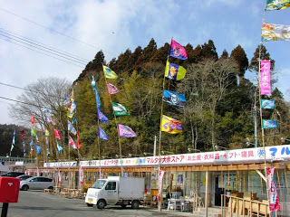 伊里前福幸商店街の店先に立てられた色とりどりのJリーグのフラッグが風になびいている様子を写した写真